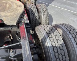 Close-up view of a truck's rear axles, showing four tires and part of the metal frame on a paved surface.