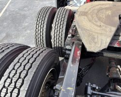 Close-up view of a truck's rear wheels and fifth wheel coupling on an asphalt surface.
