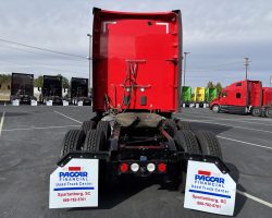 Rear view of a red semi truck cab at a dealership lot, flanked by two PACCAR Financial signs.