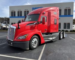 A red semi-truck is parked in a lot in front of a commercial building with blue accents.